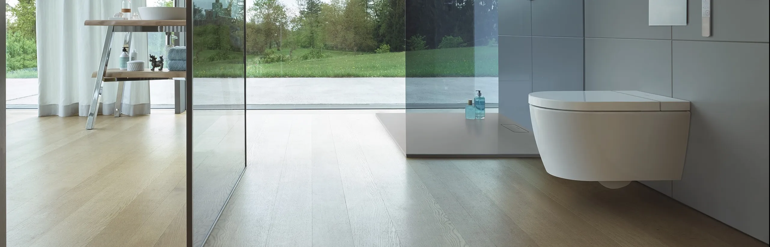 Duravit WC vor Glaswand mit geöfneter Tür und Bilck in den Garten