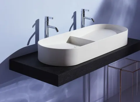 Ein modernes, ovales Waschbecken in schlichtem Weiß steht auf einer schwebenden, schwarzen Holzplatte.