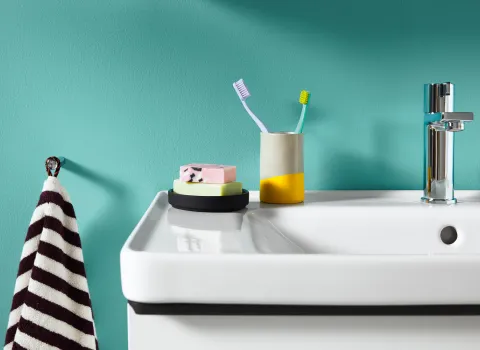 Eine Armatur der Komplettbadserie Duravit D-Neo vor türkiser Wand.