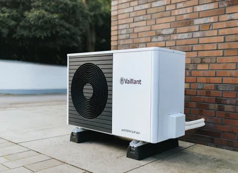 Eine Vaillant-Wärmepumpe befindet sich neben einer roten Ziegelmauer auf einem stabilen Betonfundament.