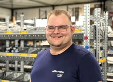 Der Anlagenemechaniker Nico von müller+sohn steht lächelnd vor einem Regal mit Werkzeug.