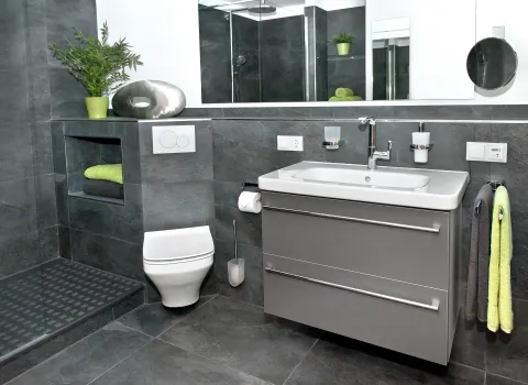 Kellerbad in Frechen mit WC, Dusche und grauem Waschtisch mit grauen Wand- und Bodenfliesen. 