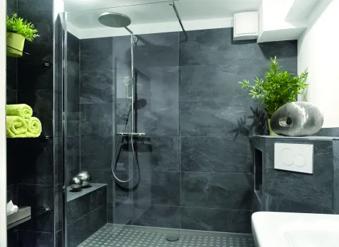 Bad mit grauen Fliesen und bodenebener Walk-in Dusche mit gefliester Sitzbank.