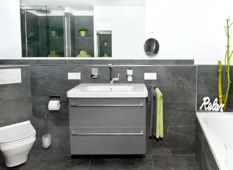 Großzügiges Badezimmer in einem Kellerraum mit grauen Fliesen, Badewanne, Waschtisch und WC