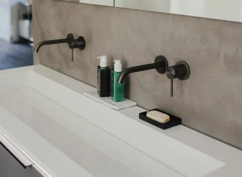 Nahaufnahme eines großzügigen Doppelwaschtischs mit zwei dunklen Unterputzarmaturen.