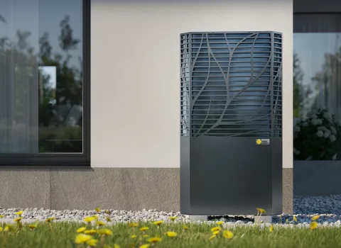 Eine moderne Luft-Wasser-Wärmepumpe steht an der Außenwand eines Einfamilienhauses auf einem mit Kies bedeckten Streifen.