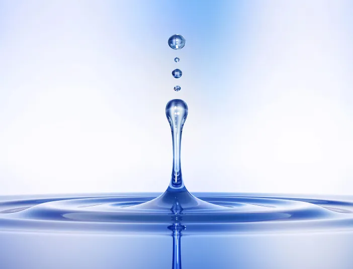 Ein Wassertropfen steigt nach dem Auftreffen auf die Oberfläche empor, umgeben von kleineren Tropfen in der Luft.