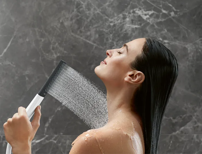 Eine Frau mit nassen, nach hinten fallenden Haaren hält eine moderne Handbrause und richtet den Wasserstrahl auf ihren Nacken.